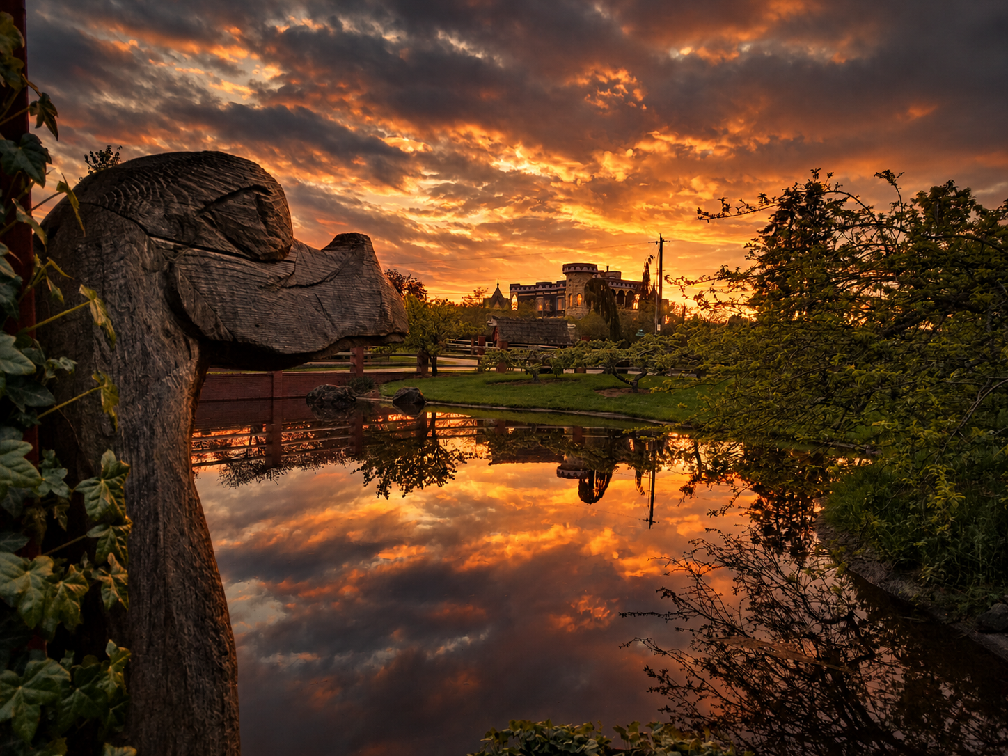 The castle, pond, and wooden troll sculpture at sunset